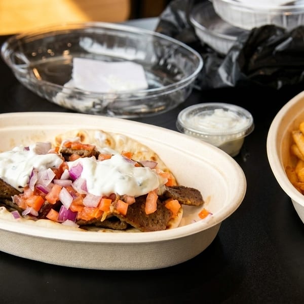 Gyro with tzatziki, tomatoes, and onions, alongside a bowl of french fries and sauce.