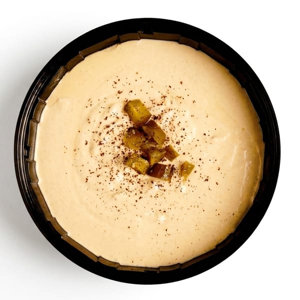Overhead view of a black bowl filled with creamy hummus, topped with diced green peppers and spices.